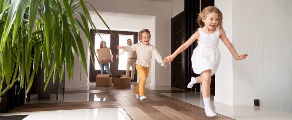 Horizontal photo happy little kids running into new home, parents with cardboard boxes on background. Loan mortgage, moving relocating concept banner for website header design with copy space for text